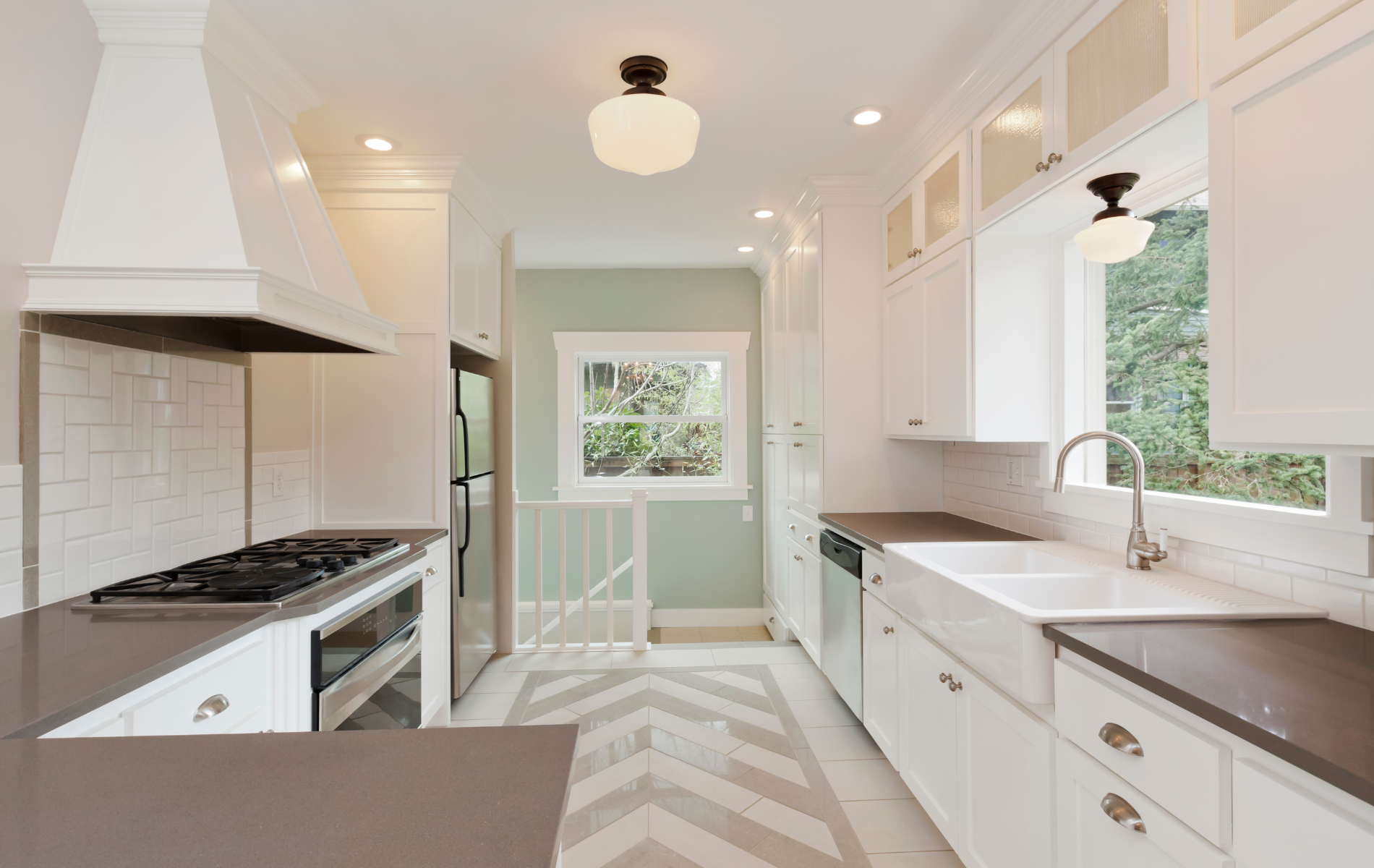 A kitchen with white cabinets , a stove , a sink , and a window.