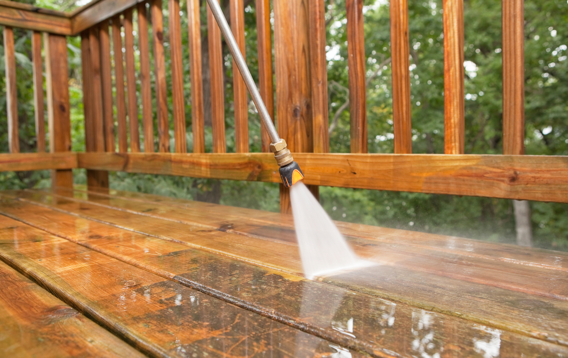 A person is using a high pressure washer to clean a wooden deck.
