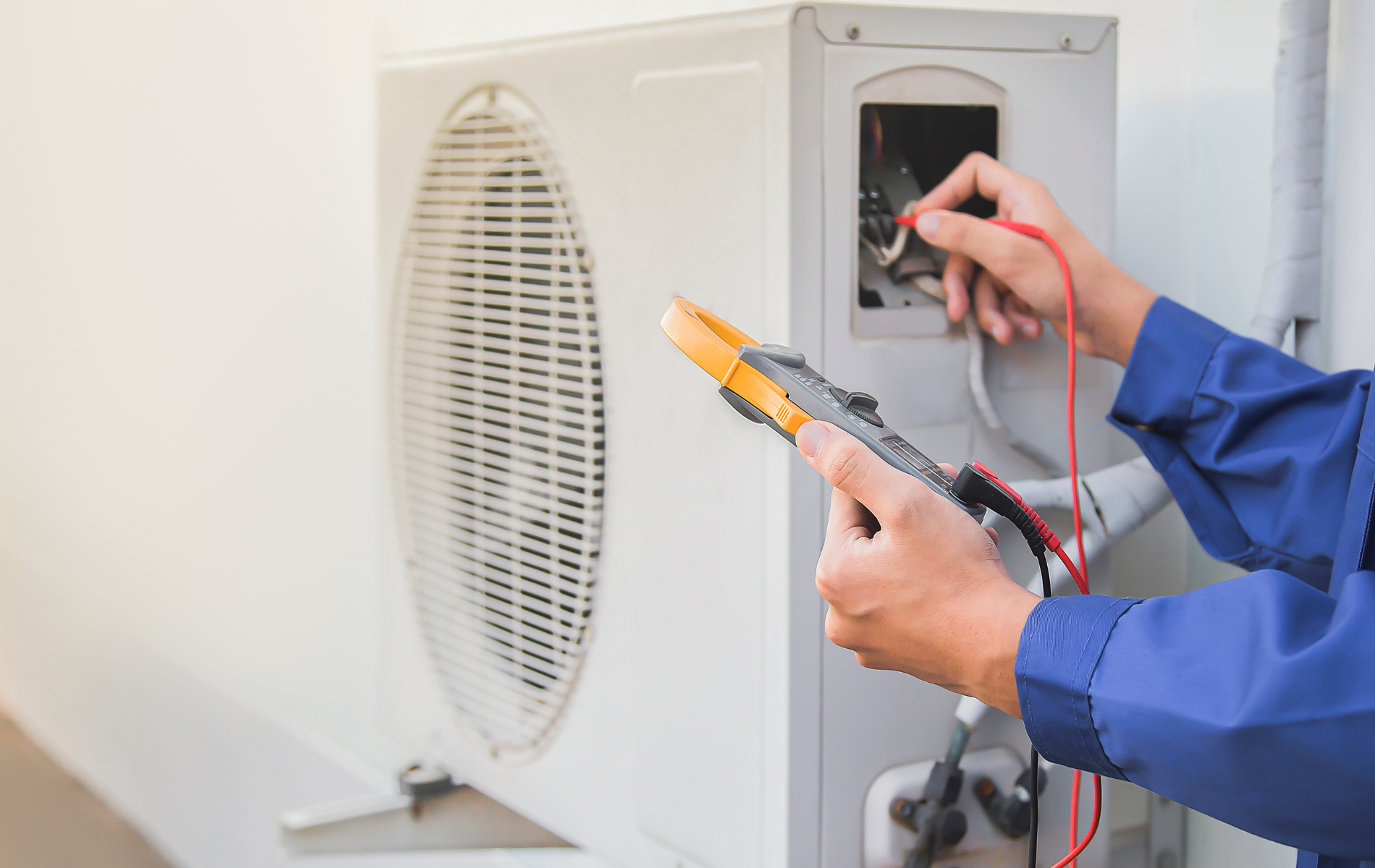 A man is fixing an air conditioner with a multimeter.
