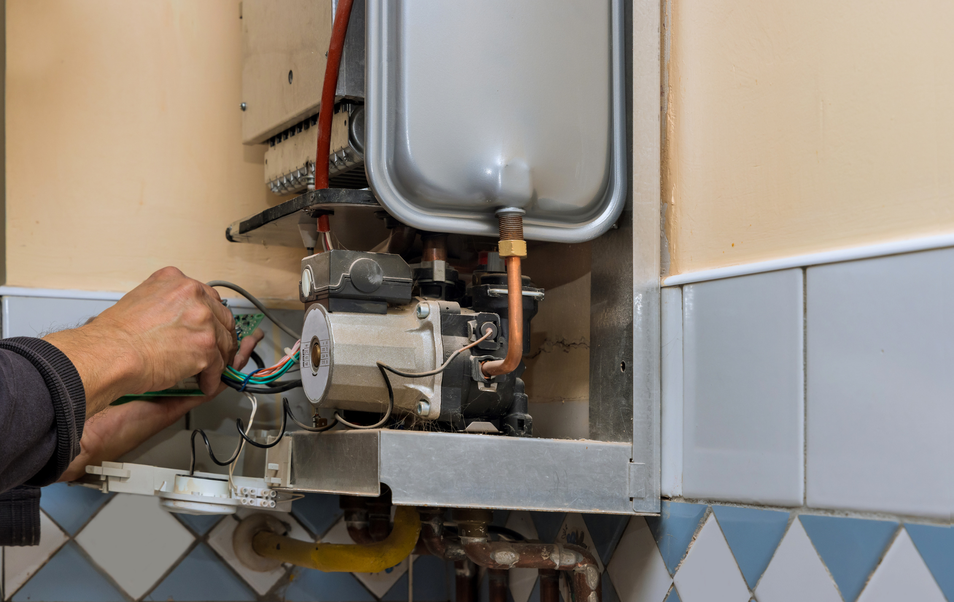A person is fixing a boiler in a kitchen.