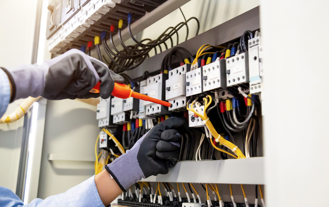 An electrician is working on an electrical box with a screwdriver.