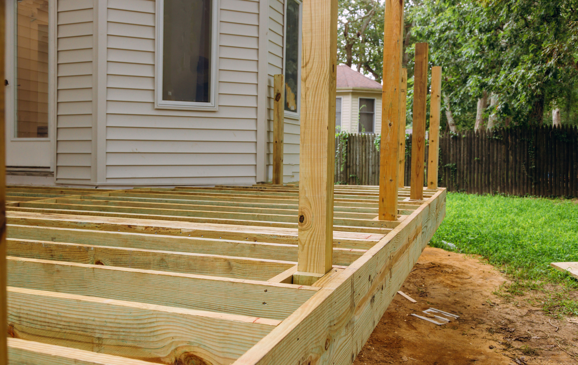 A wooden deck is being built in front of a white house.