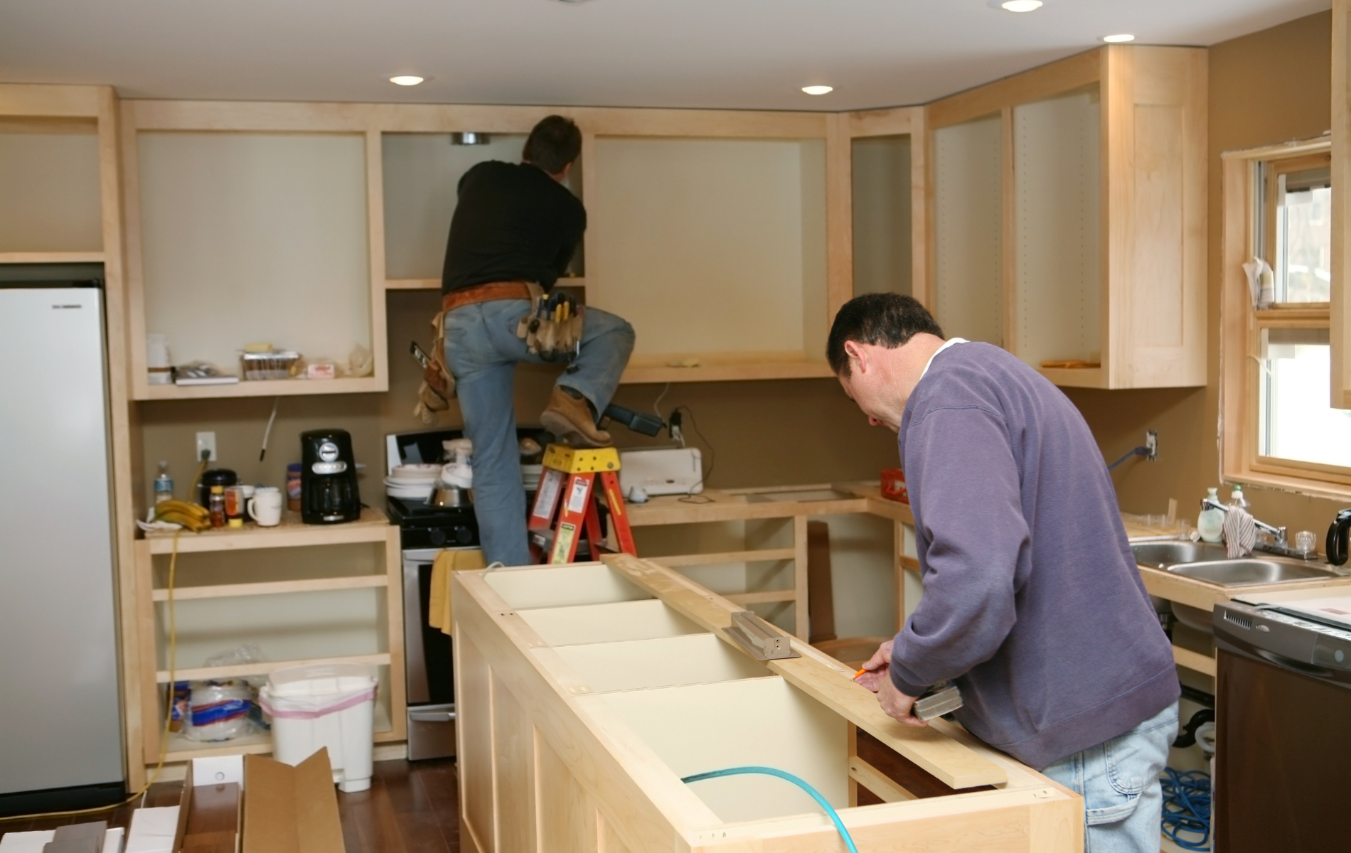 Two men are working on a kitchen with a ladder