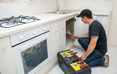 A man is kneeling down in a kitchen with a toolbox.