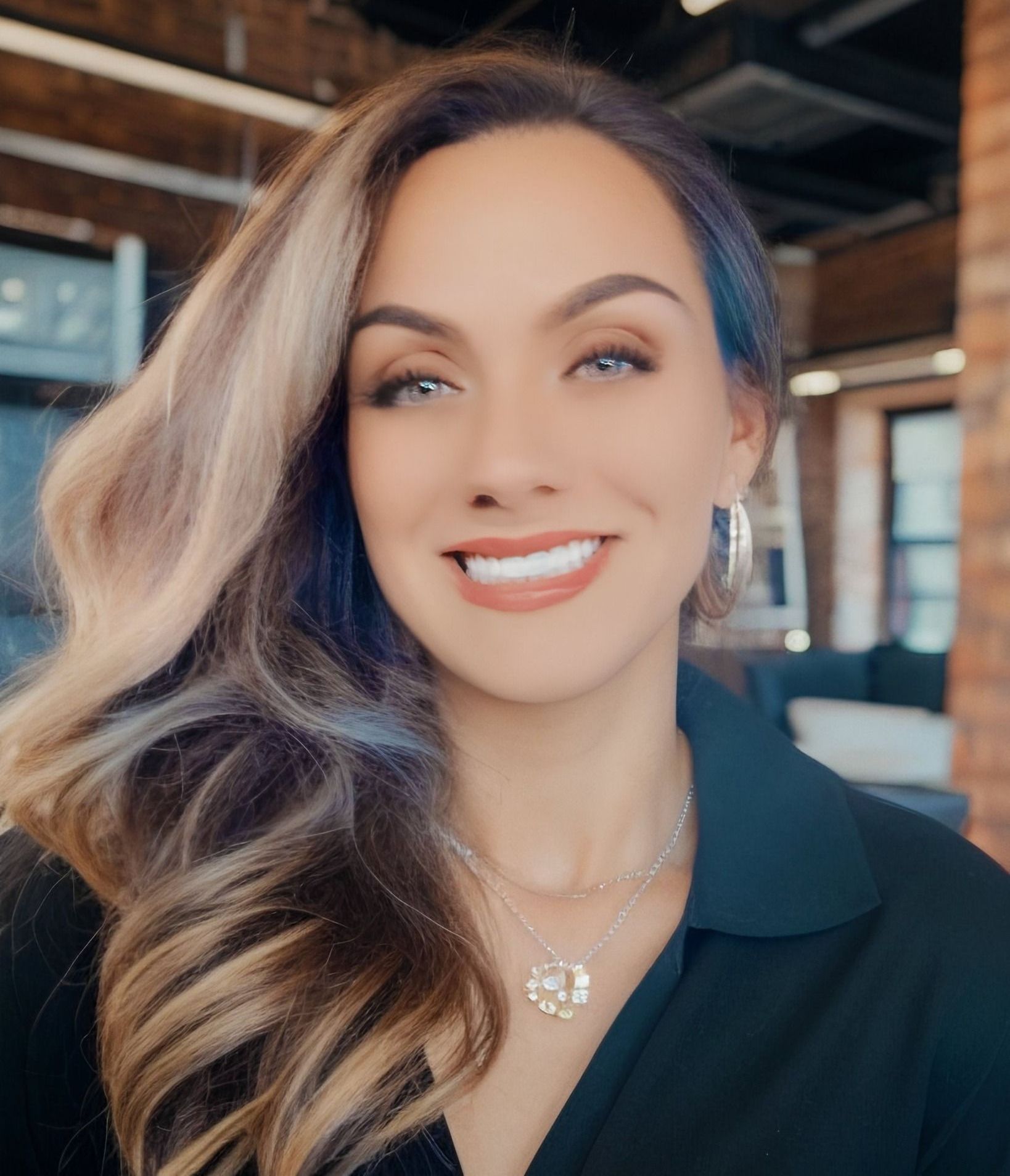 A woman wearing a black shirt and a necklace is smiling for the camera.