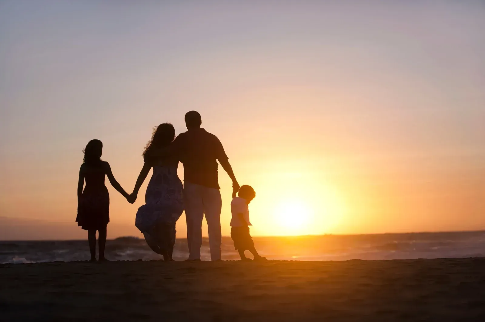A family is standing on a beach at sunset holding hands.
