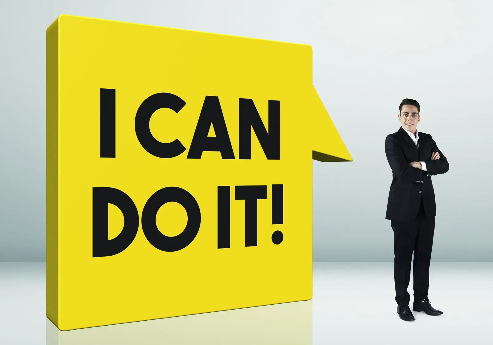 A man in a suit stands in front of a yellow sign that says i can do it