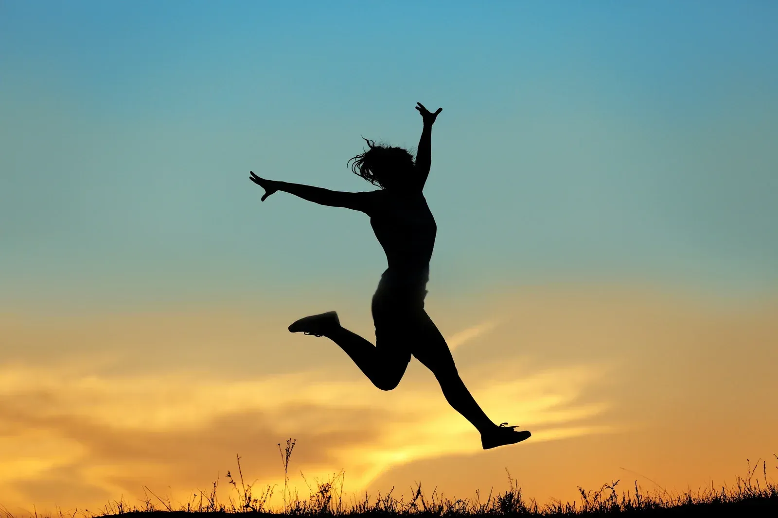 A silhouette of a woman jumping in the air at sunset