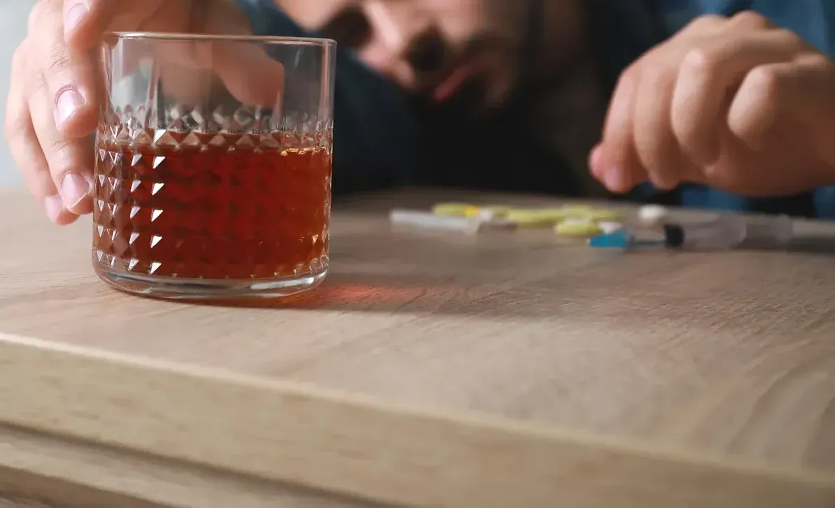 Cigarettes , pills , a glass of water and a shot glass on a wooden table.