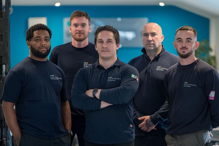 A group of five men in navy shirts posing. Indoor setting with blue wall, serious expressions.