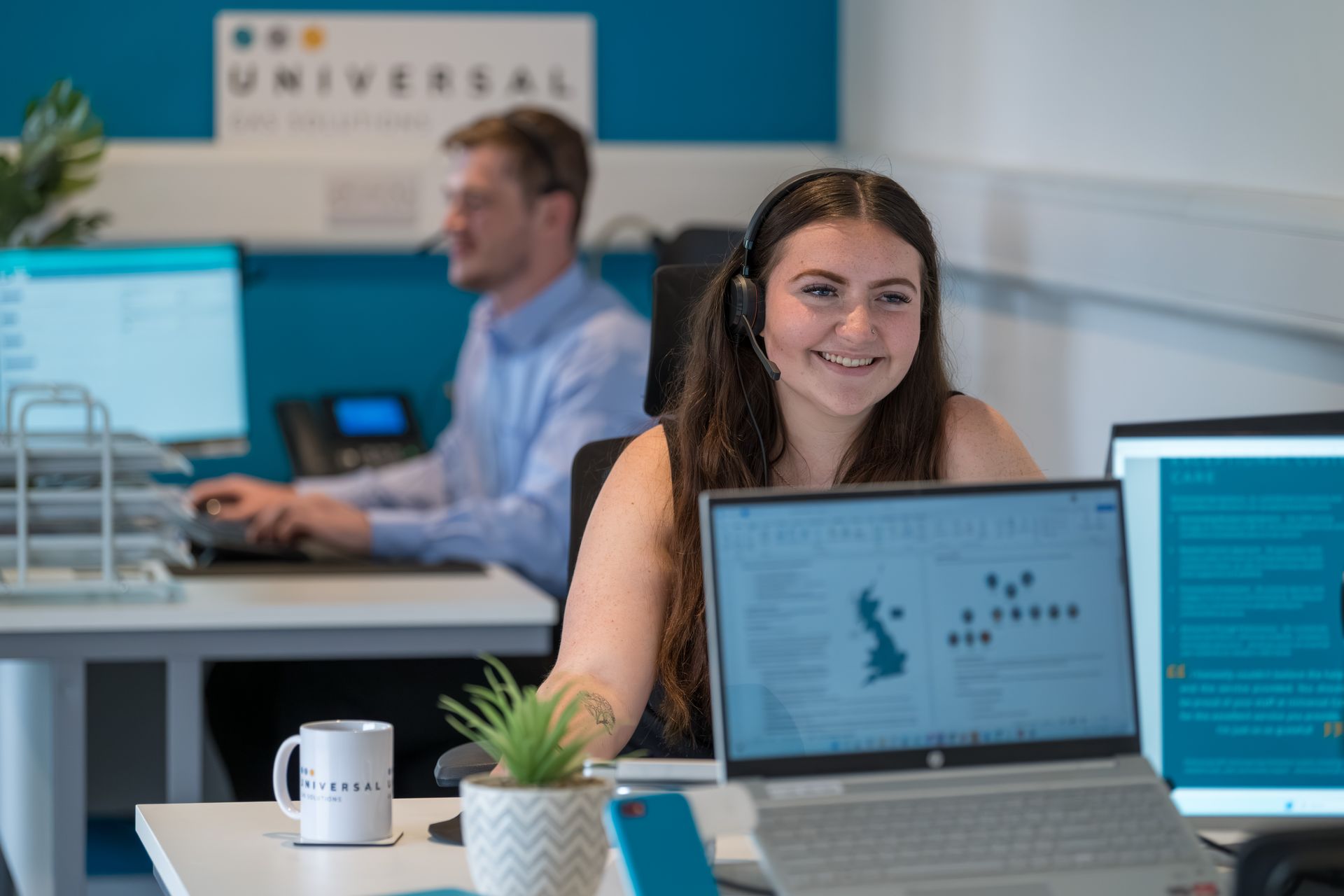 Five business professionals in an office, smiling at the camera; two women on either side, and a man in the center.