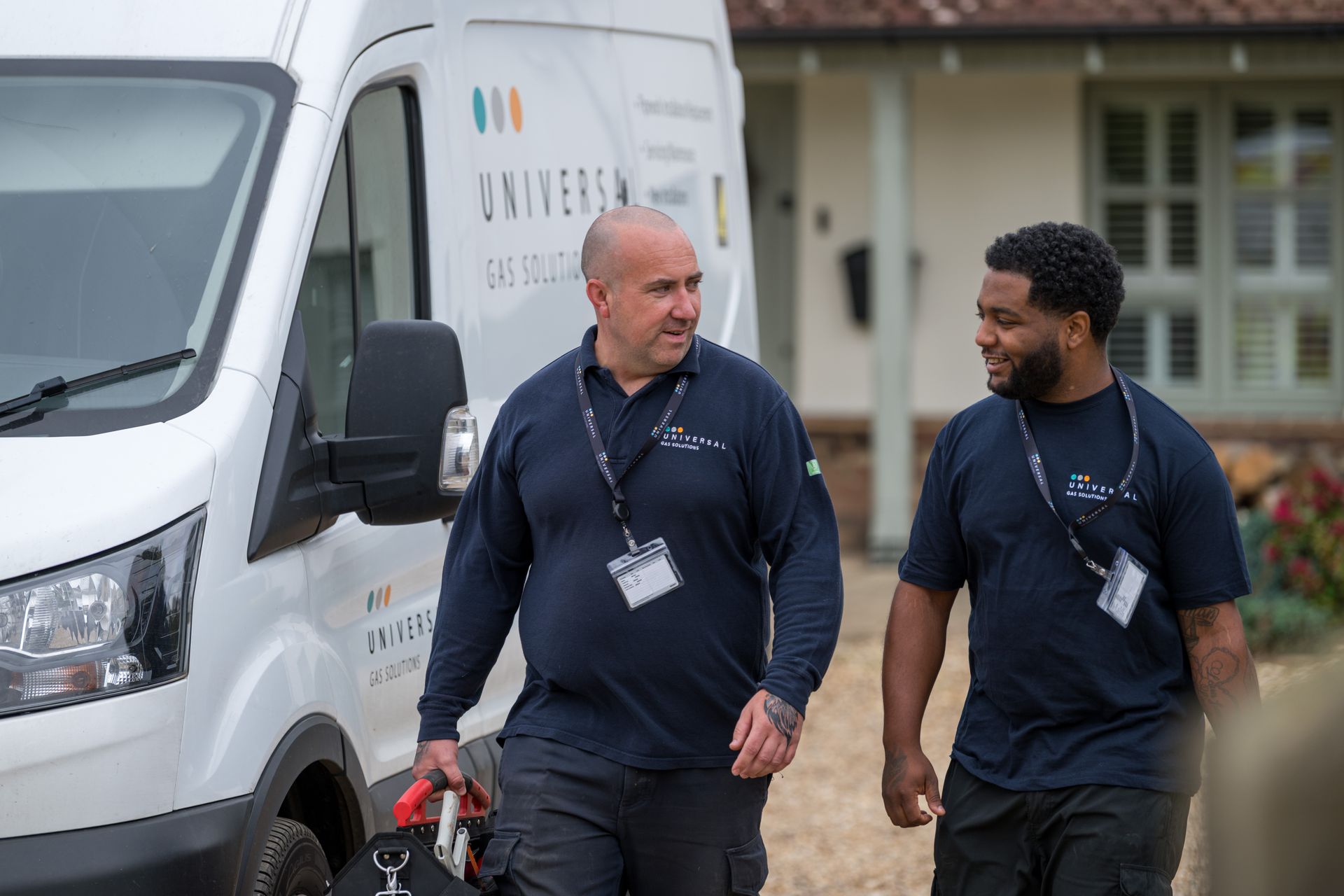 Two men in work uniforms walk near a van, likely for a gas company.