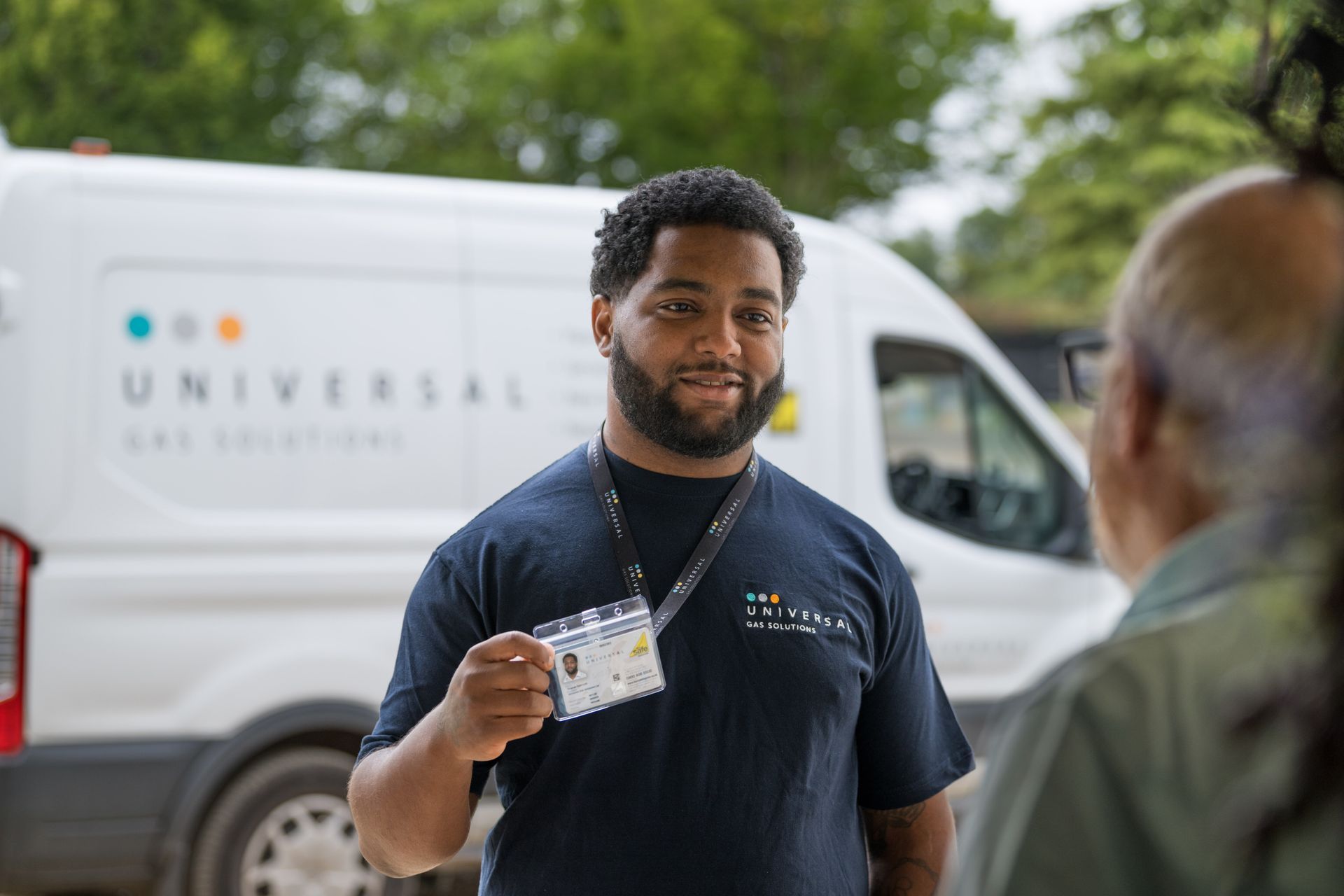 A man in blue sweater examines a boiler with a screwdriver. Indoors, light-skinned, with tattoos.
