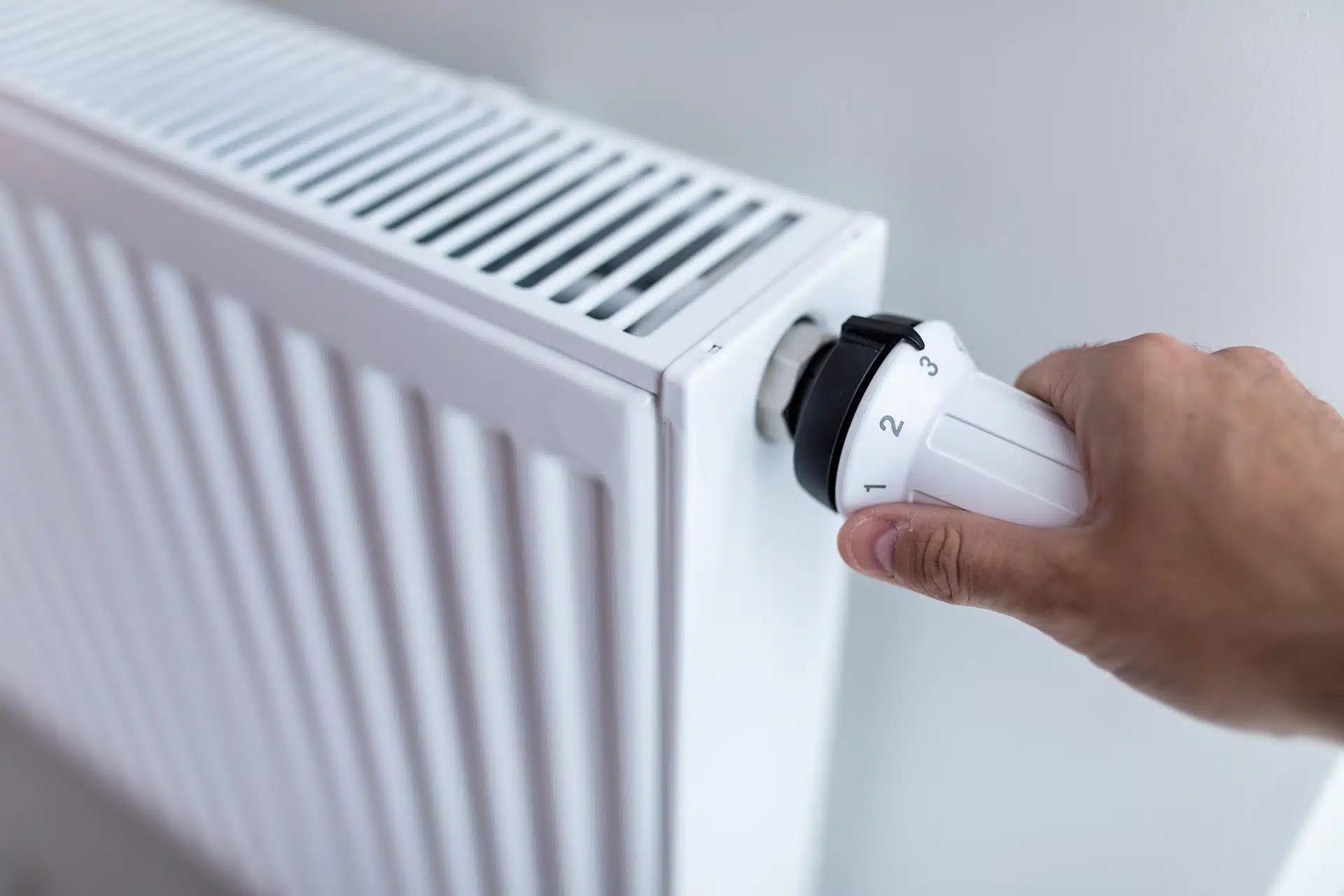 Hand turning a white radiator valve to adjust the heat setting.