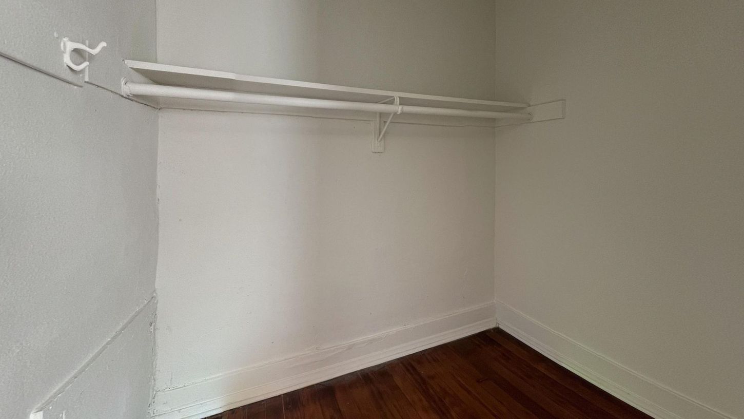 Empty closet with white shelves and rod, white walls, and wood floor.