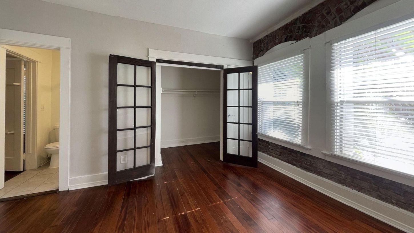 Empty room with hardwood floors, closet, French doors, and windows with blinds.