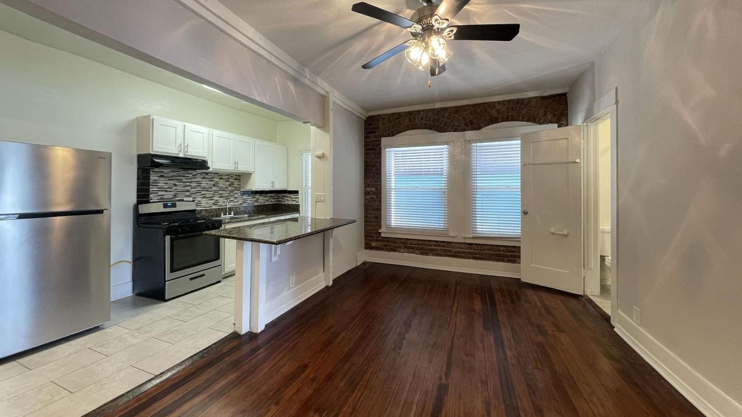 Interior view of a renovated apartment with open kitchen, dark wood floors, and exposed brick.