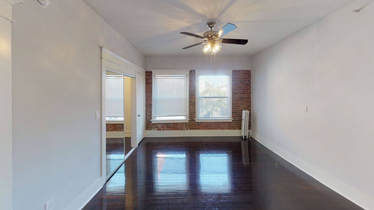 Empty room with dark wood floor, exposed brick, and a ceiling fan.
