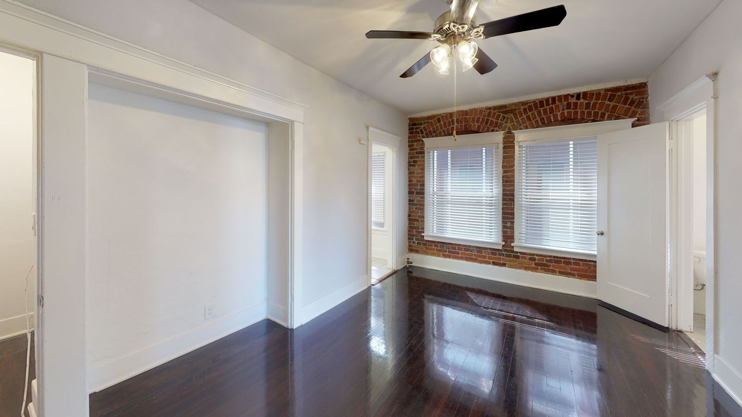 Empty room with dark wood floor, exposed brick wall with windows, and white trim.