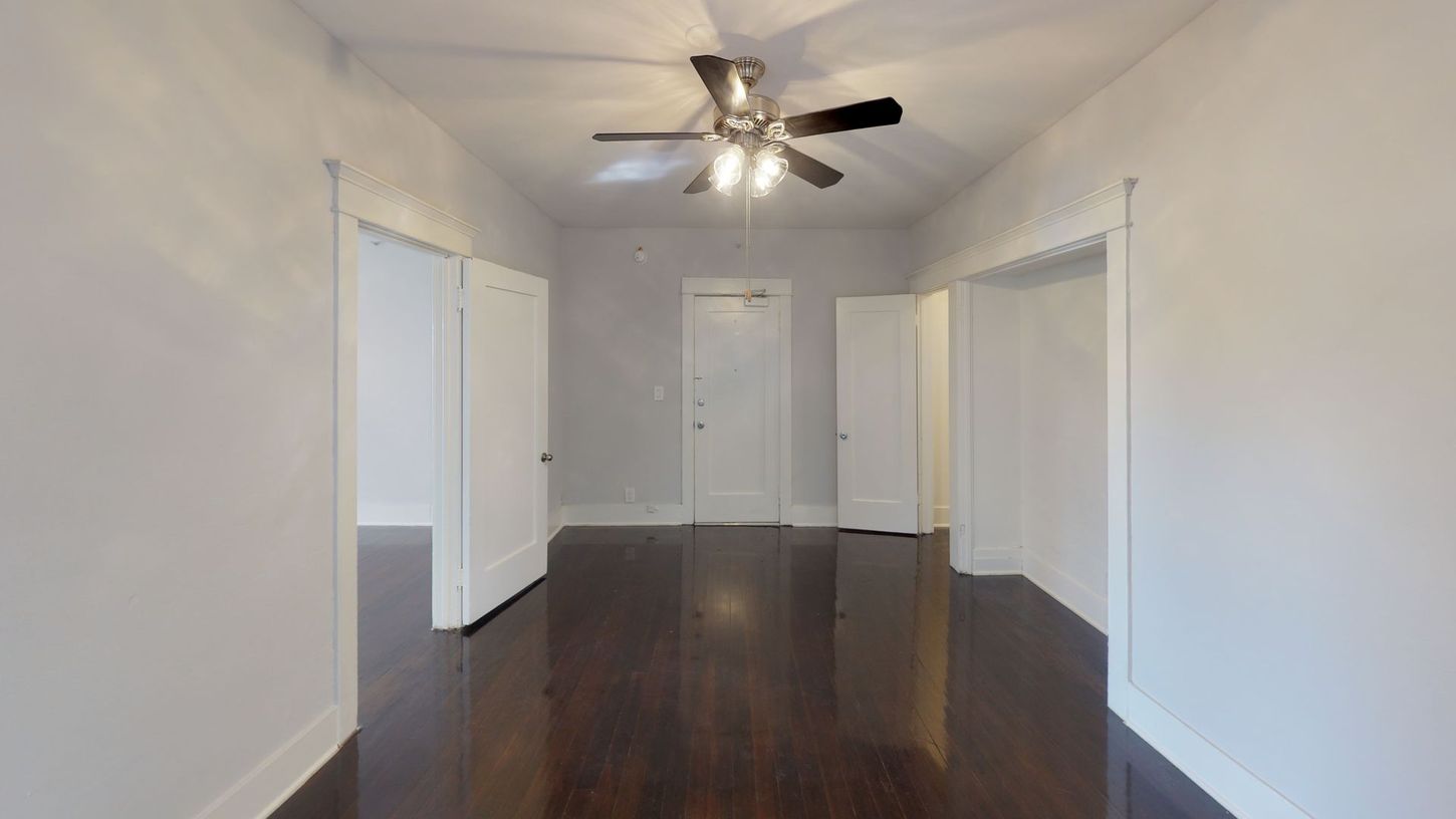 Empty room with dark wood floors, white walls, multiple white doors, and a ceiling fan.