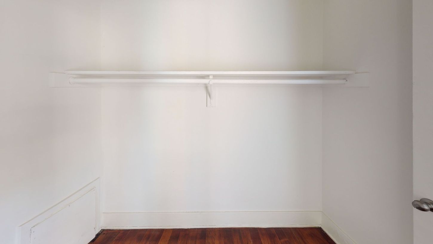 Empty white closet with a rod and wood floor.