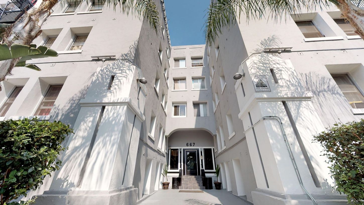 Gray apartment building with arched entrance and palm trees.