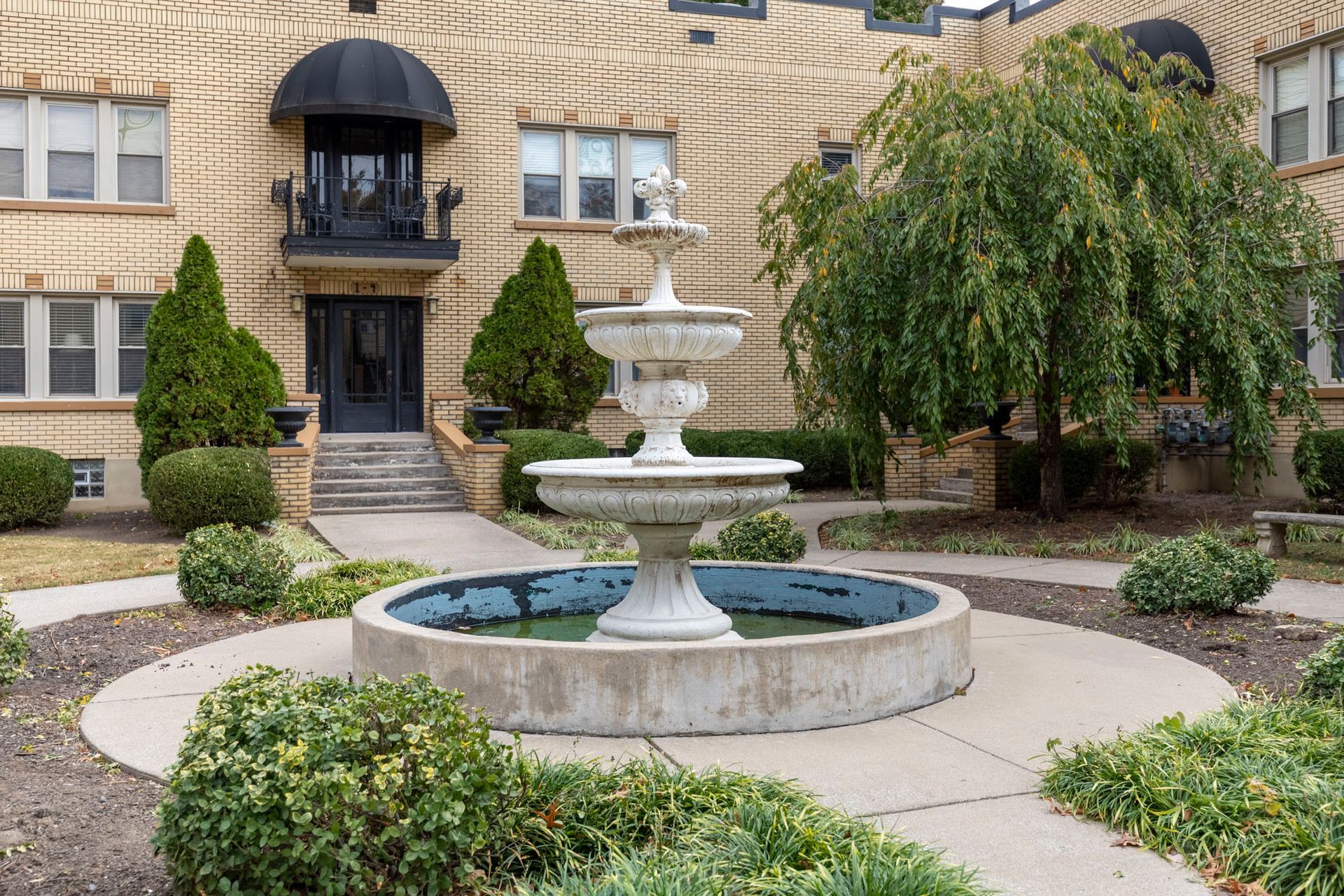 A fountain is in the middle of a courtyard in front of a brick building.