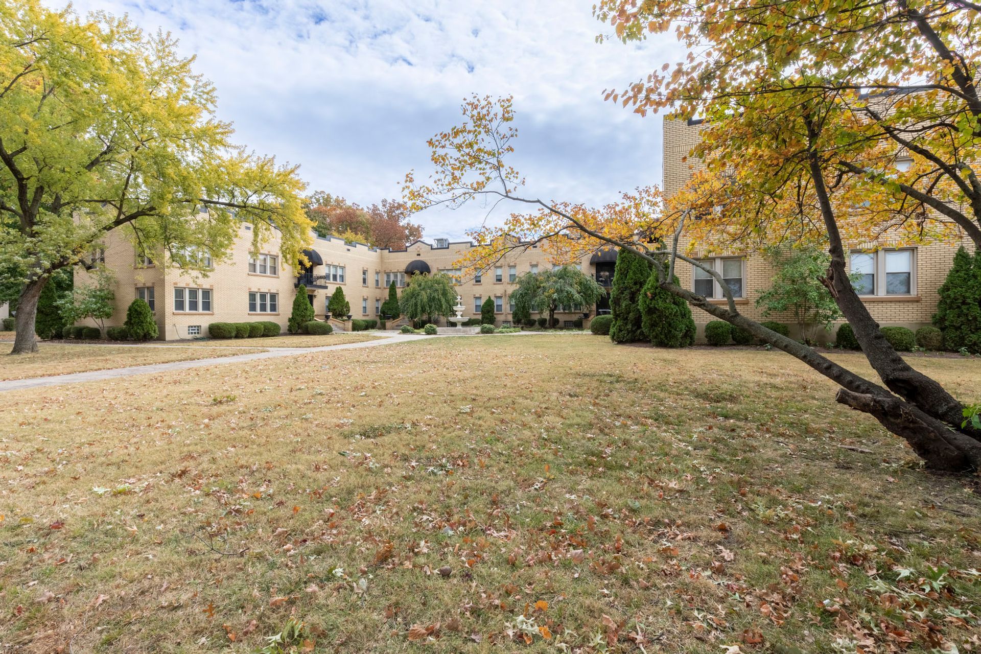 A large grassy field with trees and buildings in the background.