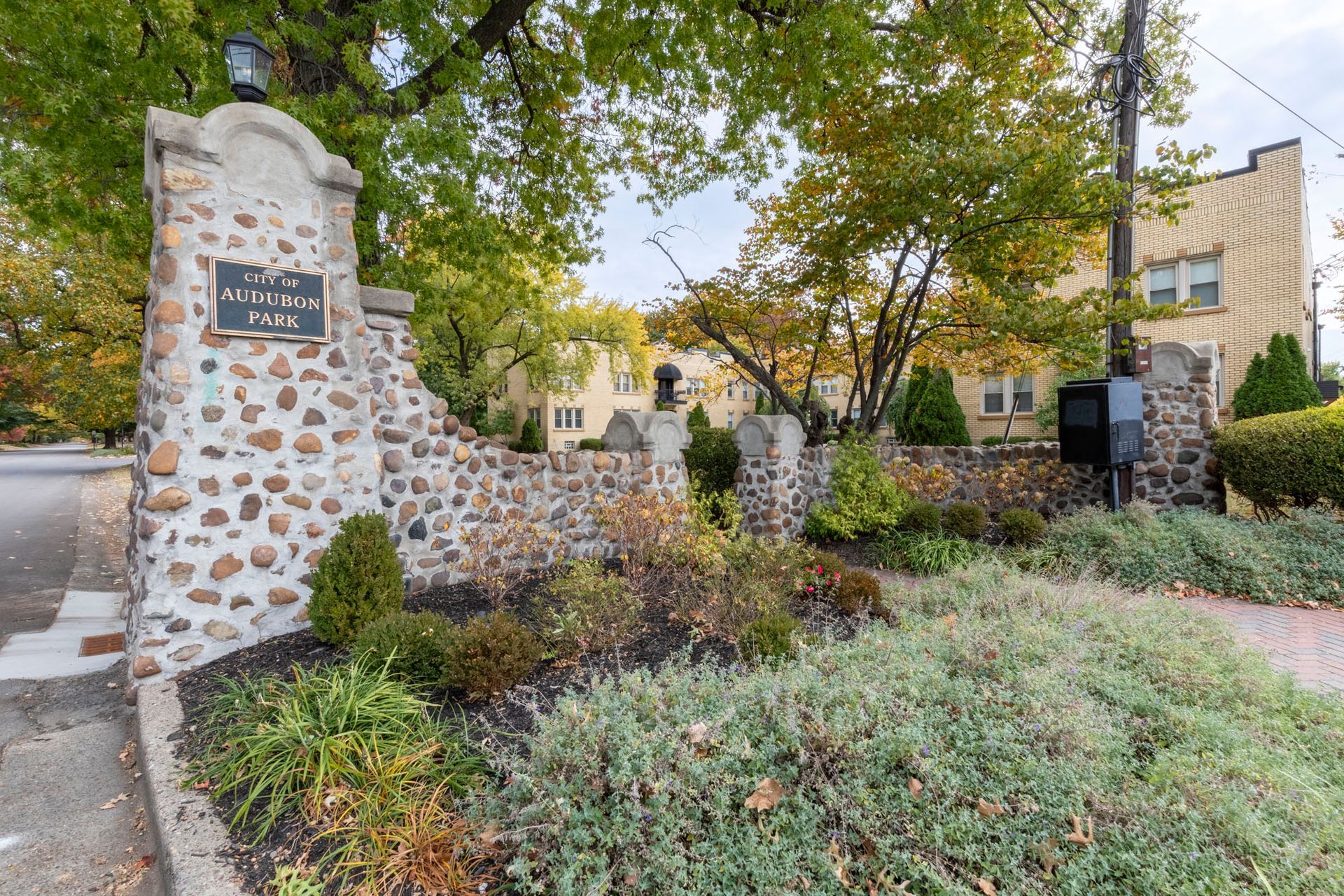 A stone wall with a sign on it is surrounded by trees and bushes.