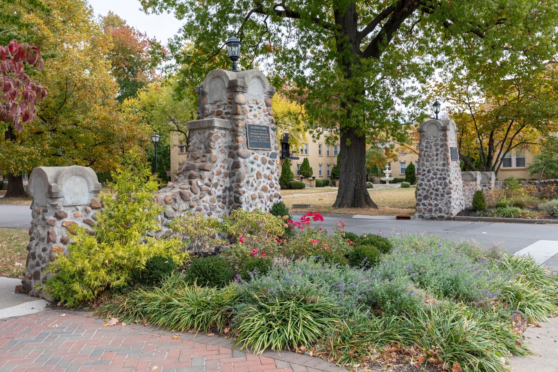 A stone entrance to a park with trees and bushes
