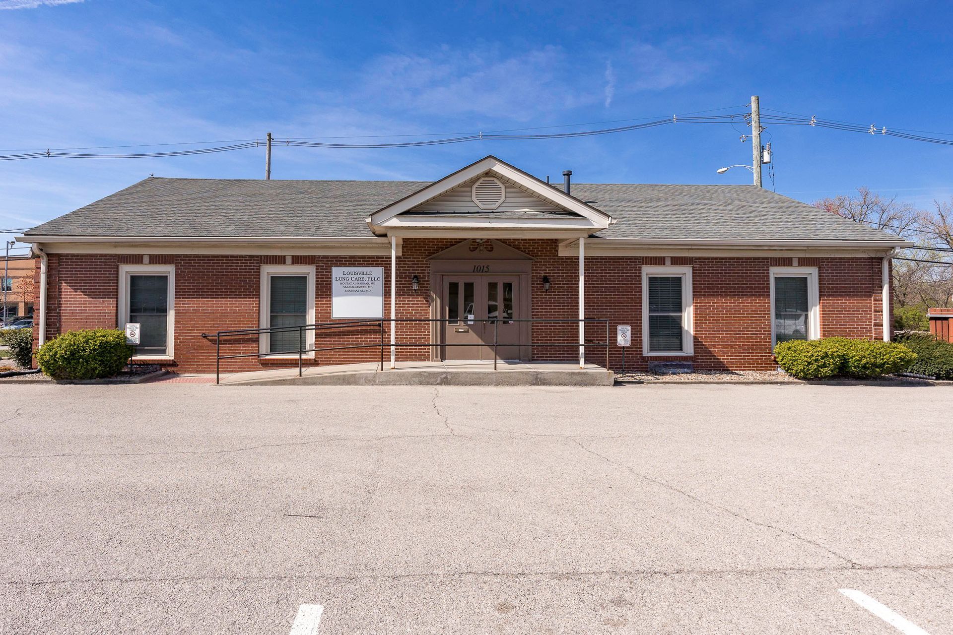 A small brick building with a gray roof and a parking lot in front of it.