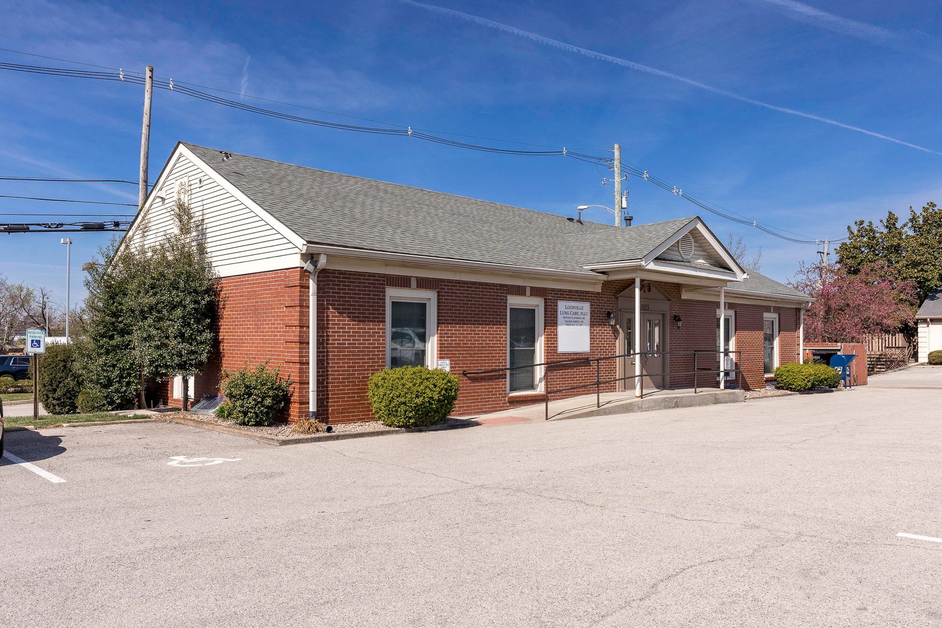 A small brick building with a gray roof and a parking lot in front of it.
