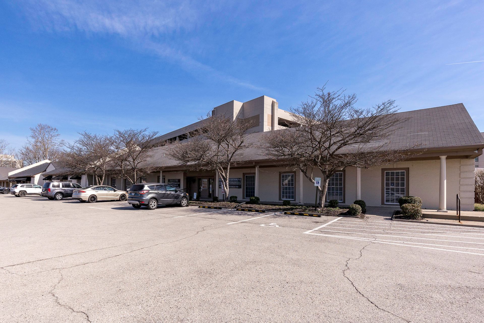 A small white building with a lot of windows is sitting next to a parking lot.