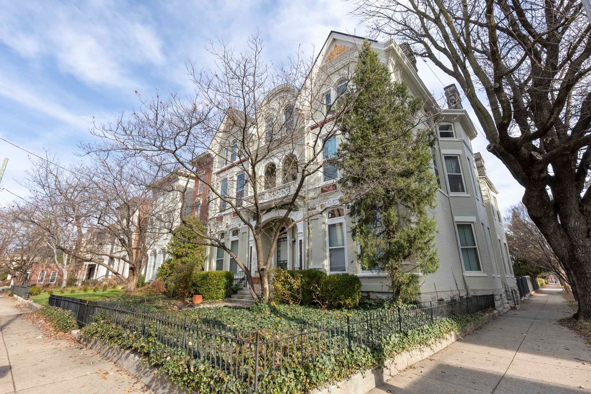 A large white house with a fence and trees in front of it.