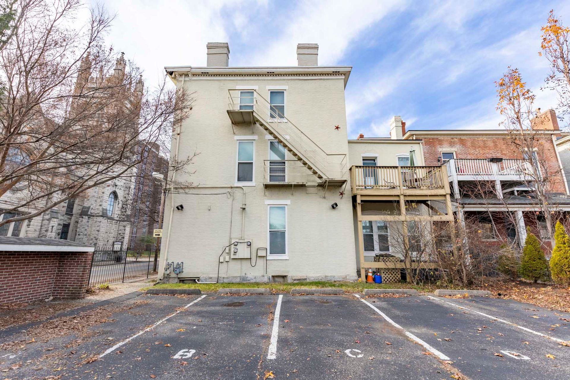 A large white building with a fire escape and a parking lot in front of it.