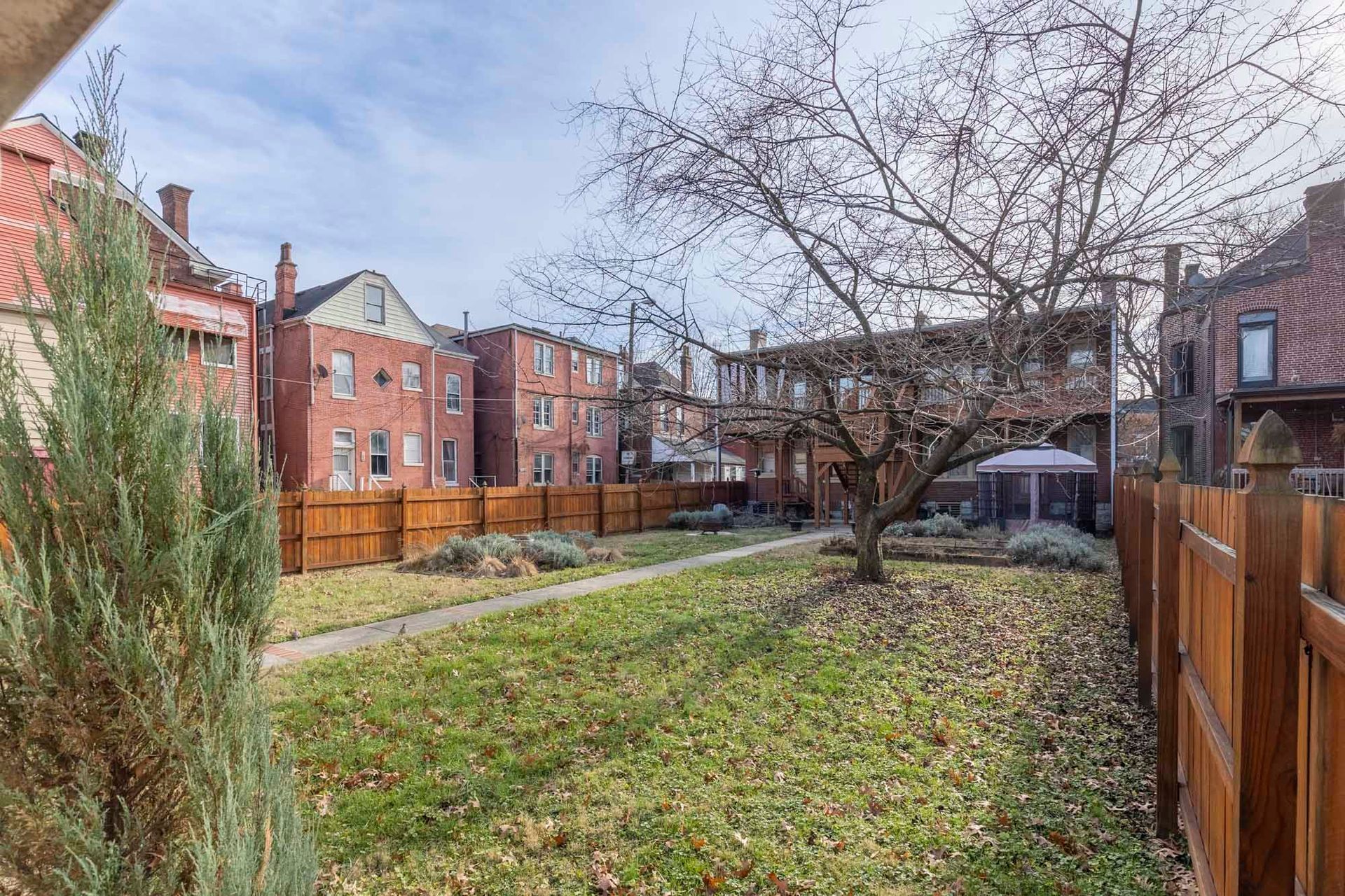 a backyard with a wooden fence and a tree in front of a brick building .