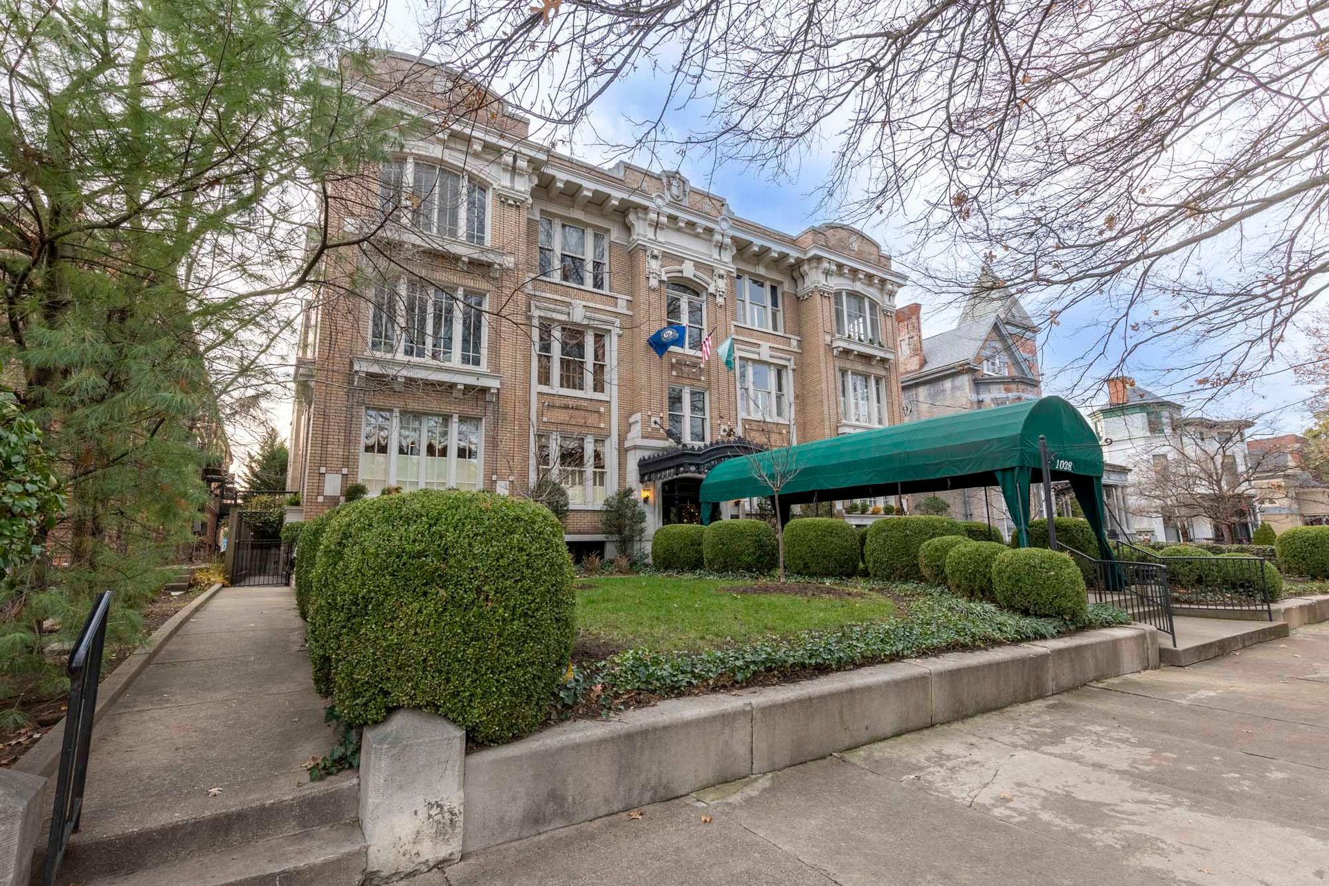 a large building with a green awning is surrounded by bushes and trees .