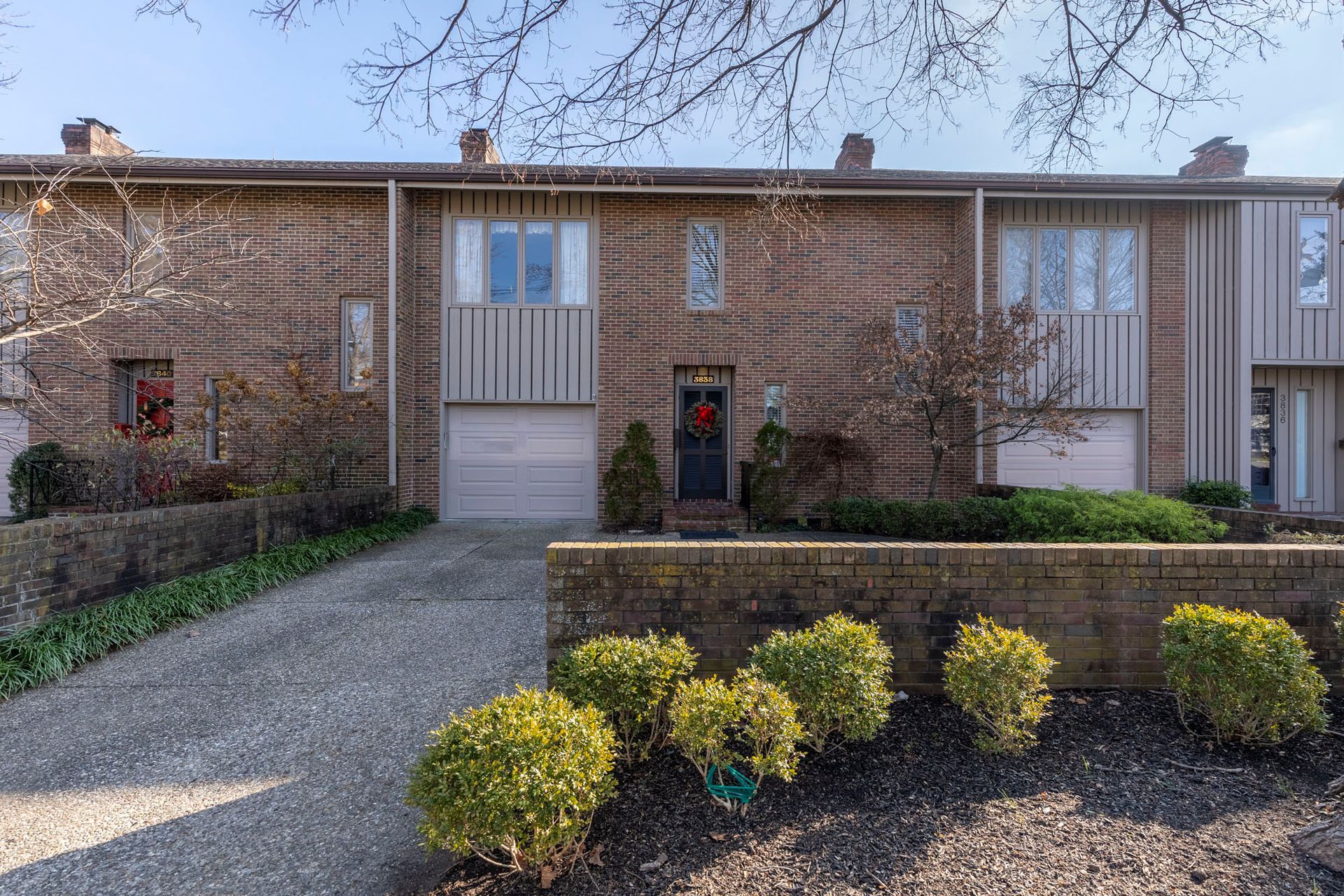 A brick house with a driveway and bushes in front of it.