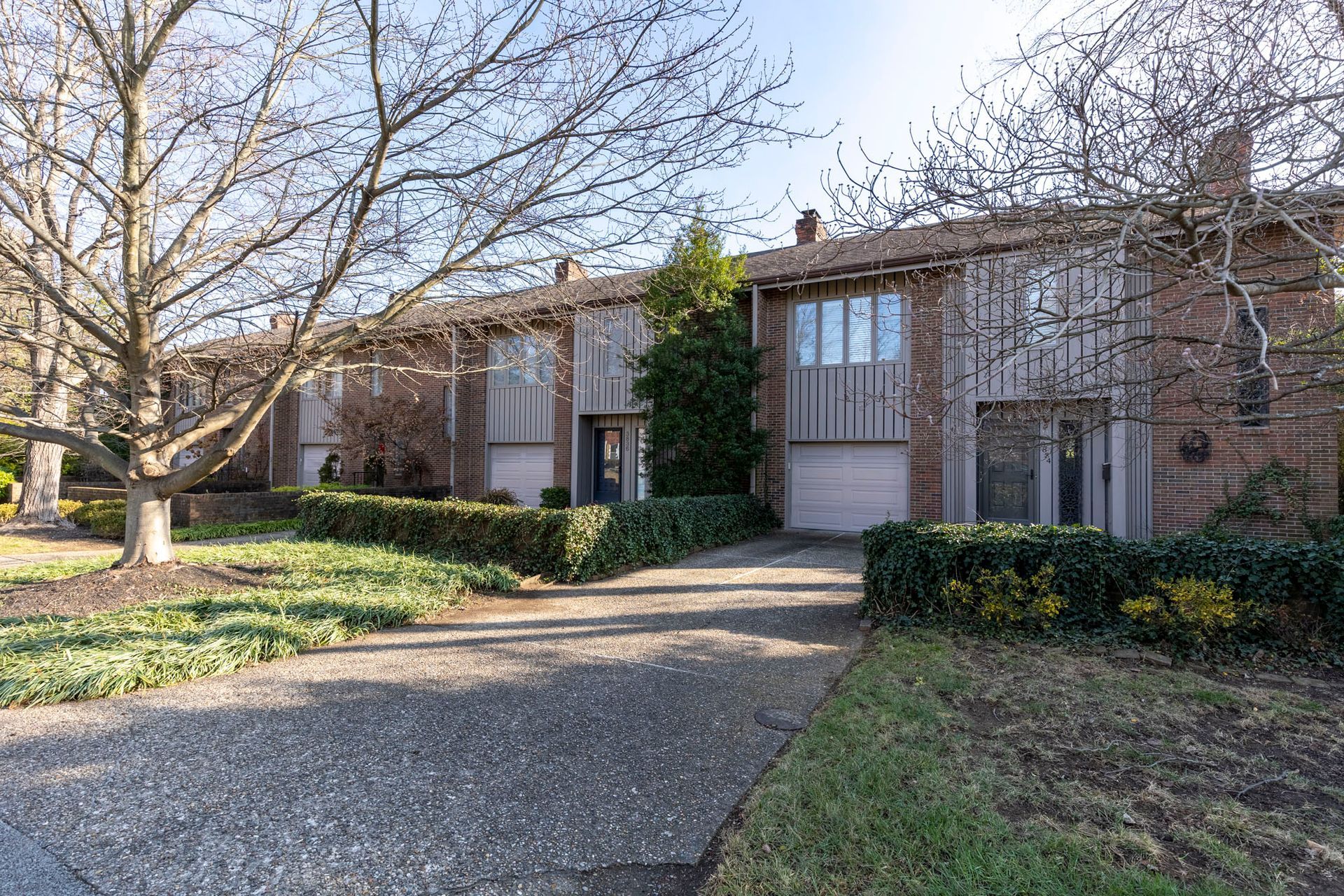A row of houses with a driveway and trees in front of them.