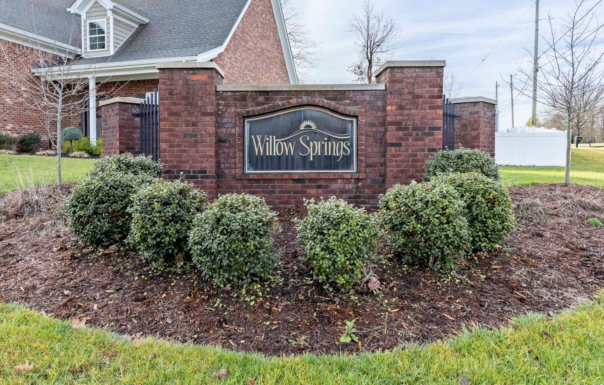 a sign for willow springs is surrounded by bushes and mulch in front of a brick building .