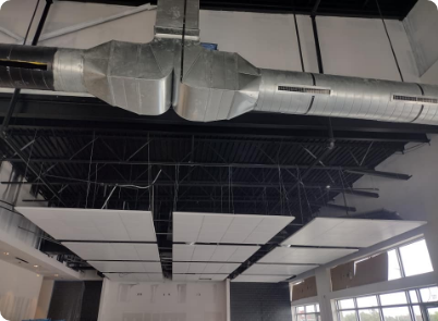 Construction site interior with exposed black beams, ductwork, and white ceiling tiles.
