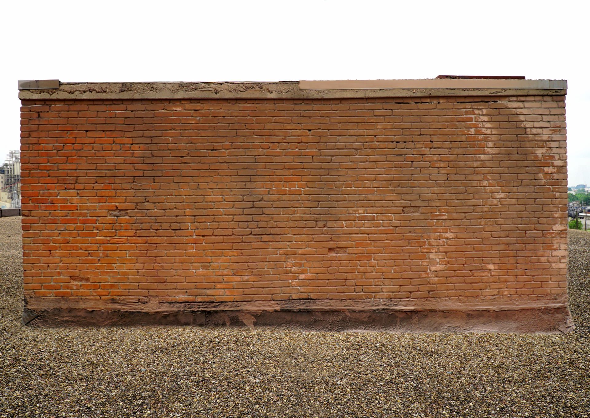 A large brick wall is sitting on top of a gravel field.