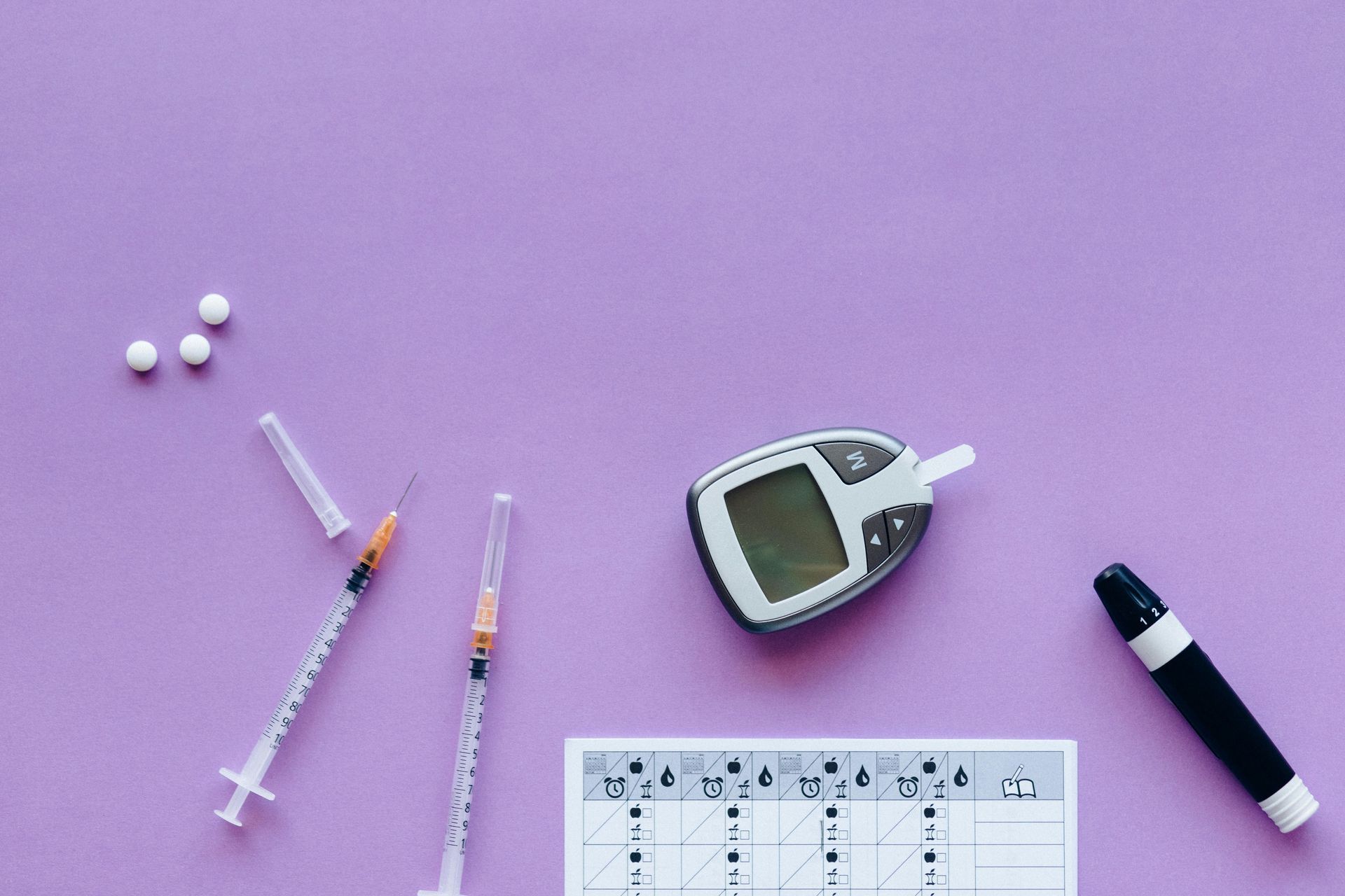Diabetes care supplies on a purple background: syringes, glucose meter, test strips, pills, and lancet device.