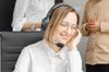 Woman with glasses and a headset smiles while working at a desk, two colleagues in the background.
