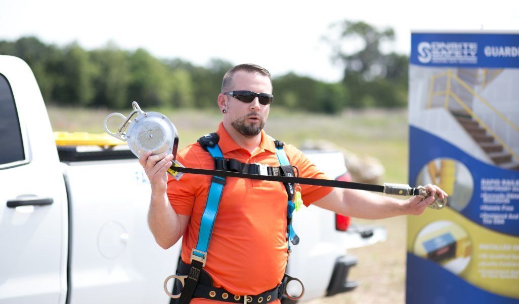 A man wearing a safety harness is standing in front of a white truck.