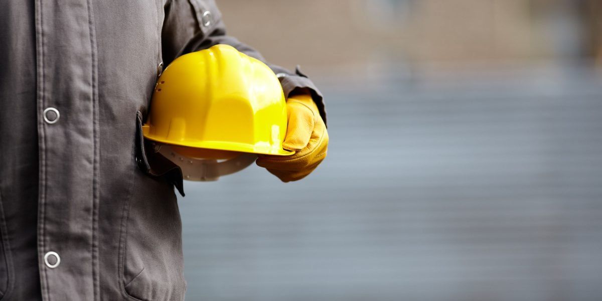 A construction worker is holding a yellow hard hat in his hands.