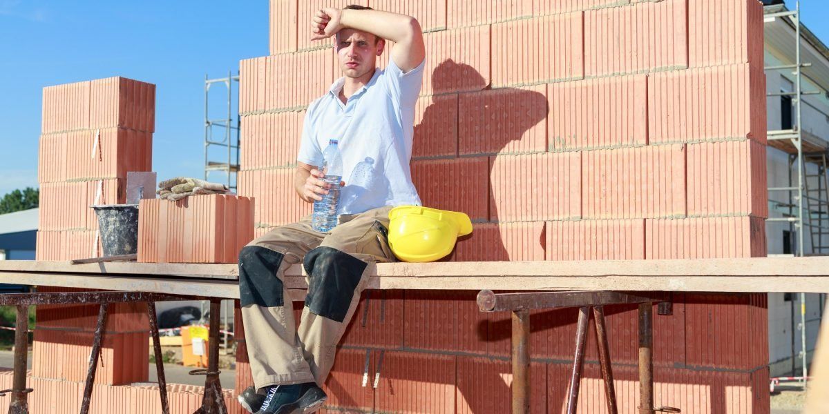 A construction worker is sitting on a wooden table in front of a brick wall.