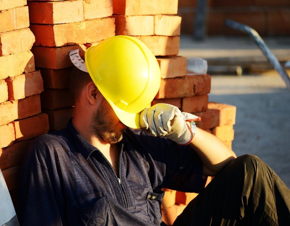 A man wearing a hard hat is leaning against a brick wall