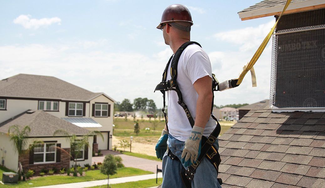 A man wearing a hard hat and safety harness is standing on top of a roof.
