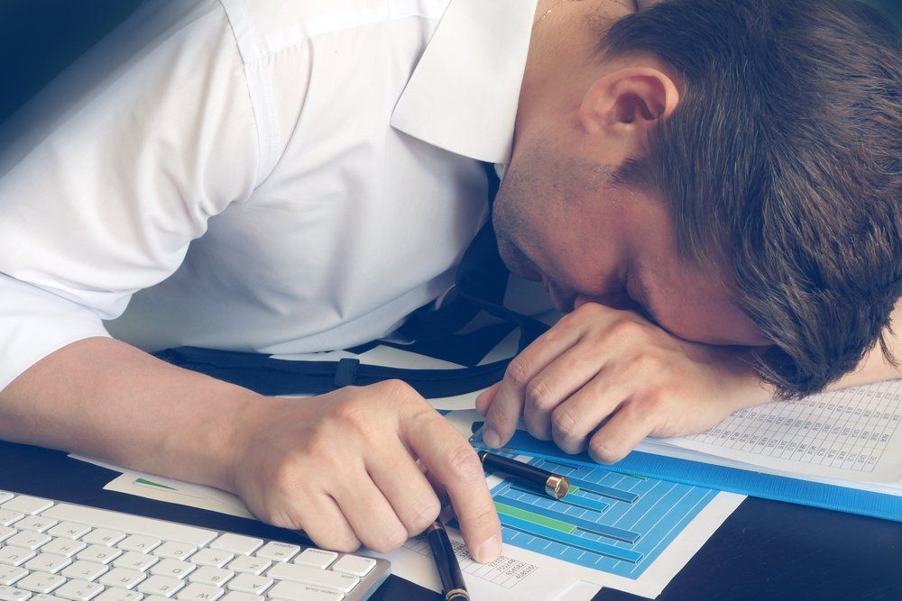 A man is sleeping at a desk with his head on the desk.